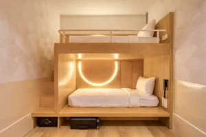 Modern minimalist hotel room with a wooden bunk bed and illuminated lighting.