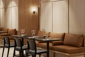 Modern restaurant interior with brown wooden walls and cushions, wooden tables with wine glasses, and black and gray cushions