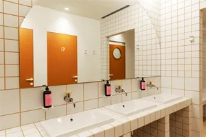 Modern restaurant interior with white tiles, orange mirrors, and industrial-style sinks.