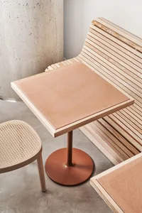 A modern restaurant interior featuring a wooden table with a cork surface and a bench seat with a wooden slat design.