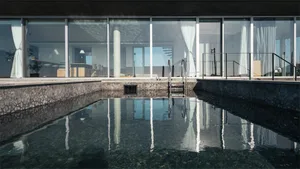 Modern residential swimming pool with concrete edges and glass walls.