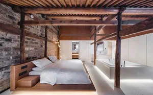 Modern bedroom featuring a wooden bed frame, white bedding, and concrete flooring with exposed brick walls.