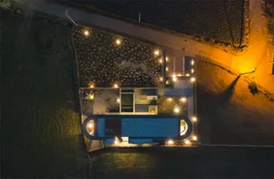 Aerial view of a modern poolhouse with concrete walls and a swimming pool at night, illuminated by outdoor lighting.