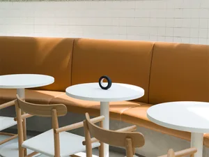Modern cafe setting with white tables, wooden seats, and brown leather cushions.