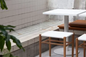 A minimalist cafe interior featuring a tiled bar counter and wooden bar stools.
