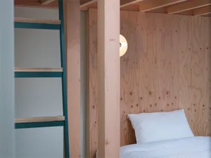 A modern minimalist bedroom featuring a wooden bed and wall panels, with a white pillow and a small round light fixture.