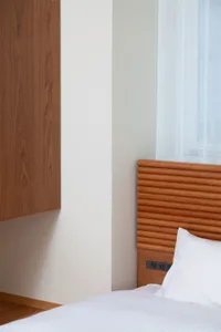 A modern bedroom features a wooden headboard and white blinds.