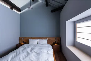 A minimalist bedroom with a modern wooden bed, white bedding, and a window with natural light.
