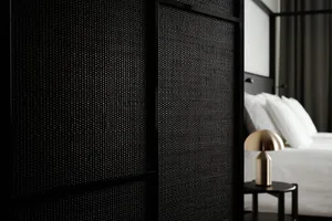 Close-up of a minimalist bedroom featuring a textured wall panel and a modern bedside lamp on a nightstand.