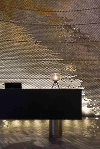 A modern lobby with metallic tiles on the walls and floor, featuring a sleek reception desk with a glass lamp.