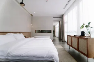 A modern minimalist bedroom with a white bed, wooden cabinet, and large windows.
