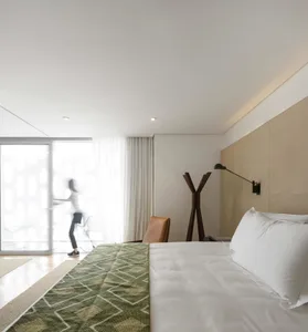 Minimalist bedroom with a textured wall, featuring a bed with white bedding and a green throw rug, and a sleek, modern design