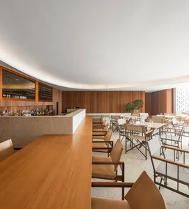 An elegant restaurant bar with wooden chairs, marble countertops, and a curved wooden wall.