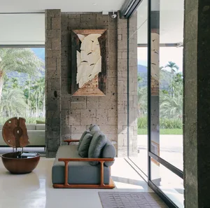 Modern living room with concrete walls, minimalist furniture, and large windows overlooking a tropical landscape.