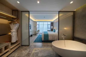 Modern hotel suite featuring a marble bathroom and bedroom area with a large bathtub and white furniture.