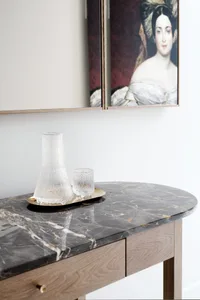 A modern vanity table with a black marble top features a glass vase and a matching glass tumbler.