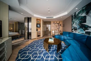 Modern living room featuring a blue sectional sofa, wooden coffee table, and glass panel divider with stainless steel accents