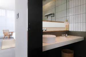 A minimalist bathroom with a white ceramic sink and tiles, featuring a floating vanity and a large window with sheer curtains