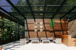 A modern patio lounge area with wooden elements, including a wooden roof supported by glass beams and wooden walls adorned wi