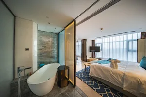 Modern residential suite featuring a bedroom, bathroom, and freestanding bathtub with a glass shower enclosure and marble fin