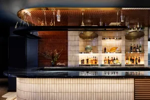 A modern restaurant bar with white and brown marble walls and flooring, featuring a circular hanging light fixture and bottle