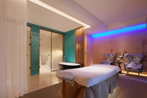 Spa treatment room with a contemporary interior design featuring white, blue, and purple lighting, a massage table, and a bat