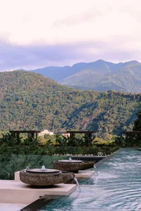 A stone water feature with water flowing into a pool, set against a backdrop of lush, mountainous scenery.