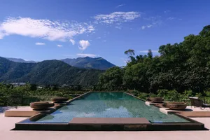 Swimming pool with tiled flooring surrounded by greenery and mountains in the background.