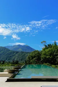 A serene pool surrounded by lush greenery with a mountain landscape in the background.