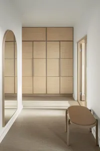 A minimalist bedroom featuring a wooden wardrobe and a cushioned bench.