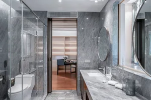 Modern residential bathroom featuring marble walls and flooring, with a glass-enclosed shower and a vanity sink area.