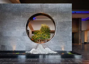 Modern hotel lobby with a circular window, tree, and water feature.