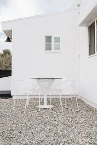 A modern patio featuring a white metal table and chairs on a gravel surface.