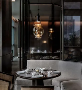 A modern restaurant interior with wooden seating, round table, and hanging pendant lights.