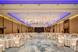 A beautifully decorated banquet hall with white fabric seats, wooden panels, glass chandeliers, and flower decorations.