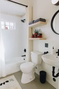 Minimalist bathroom with white wooden shelves and white ceramic toilet and sink.