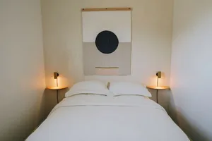 A minimalist bedroom with a white bed, wall sconces, and a geometric wall art