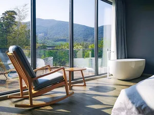A minimalist bedroom featuring wooden furniture and a large window with a view of the mountains.