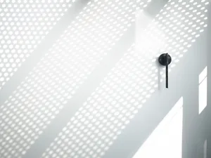 Perforated metal wall with light shining through, creating a minimalist design aesthetic.