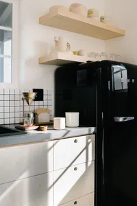 A minimalist kitchen with a black refrigerator, wooden shelves, and ceramic mugs.
