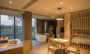 Spacious minimalist residential bathroom with a freestanding bathtub, wooden furniture, and stone flooring.