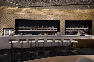 A modern bar interior with concrete and tile surfaces, featuring sleek lighting and an elegant design.