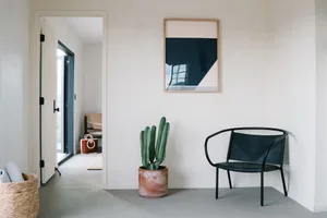 A modern, minimalist interior design featuring concrete elements, a black chair, a cactus plant, and a framed abstract art pi