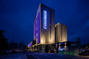 A modern conference center with a glass facade and concrete columns at night.