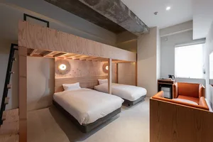 A modern hotel room featuring two beds, an orange armchair, and minimalist design elements.