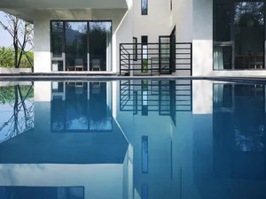 A modern house with a glass facade and concrete walls, reflecting in a pool.