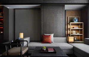 A modern living room featuring a grey sofa with red and white cushions, a black coffee table, and a wooden shelf with books a