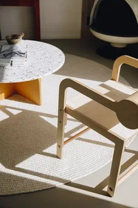 A modern living room with a circular terrazzo coffee table and a minimalist wooden chair.