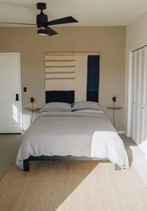 Modern minimalist bedroom with a bed, nightstands, and ceiling fan.