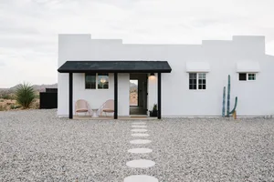 A modern, minimalist house with a white exterior, concrete walkway, and glass windows.